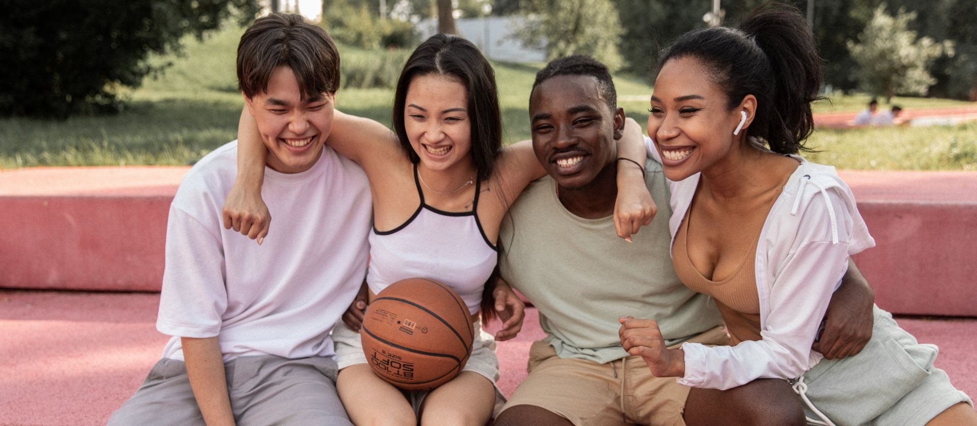 Happy multiracial friends embracing on bench after basketball training